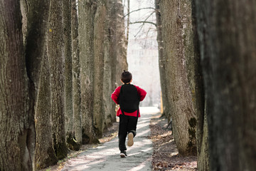 Back to school. A boy in a red sweatshirt with a backpack on his back runs down the avenue. Happy childhood in school.