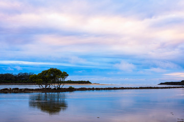 Landscape with colorful sky, ocean, trees and rocks, long exposure just after sunset shot at Urunga lagoon, Australia.