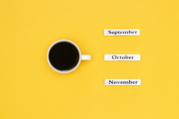 Cup of coffee and calendar November October September on yellow background