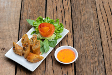 Deep fried spring rolls in a white quadrilateral dish With vegetables and tomatoes as a side dish Served on an old wooden table