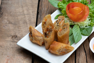 Deep fried spring rolls in a white quadrilateral dish With vegetables and tomatoes as a side dish Served on an old wooden table