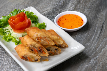 Deep fried spring rolls in a white quadrilateral dish With vegetables and tomatoes as a side dish Served on an old wooden table