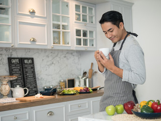 Relaxed young handsome asian man having coffee at home in kitchen.