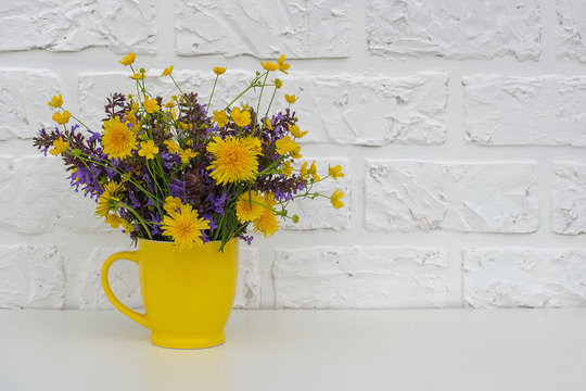 Bouquet of wild flowers in yellow cup vase on background white brick wall. Template for postcard Copy space lettering text or design Concept Women's day, Mothers Day, Hello summer or Hello spring.