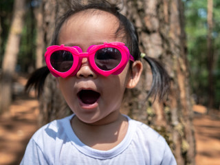 Cute Asian little child girl wearing pink glasses and white T-shirt is standing in the garden.
