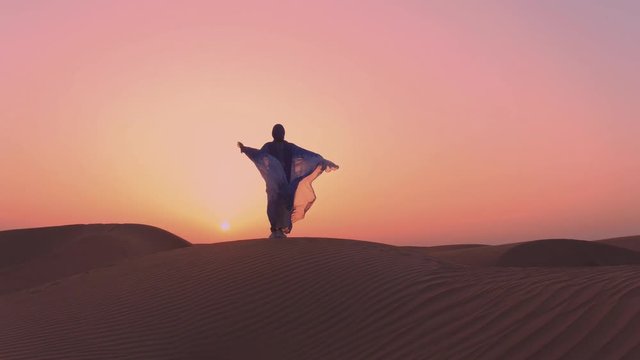 Women wearing beautiful blue and white Arab clothes rising her hands at the desert