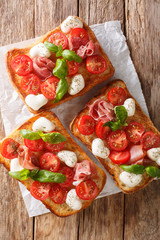 Italian open sandwiches with mozzarella, tomatoes, ham and basil closeup. Vertical top view