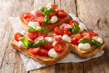 Ciabatta summer toasts with mozzarella, tomatoes, ham and basil close-up on the table. horizontal