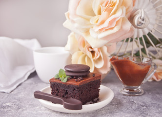 A piece of homemade chocolate cake on the plate with icing, mint leaf and chocolate spoon on the gray table