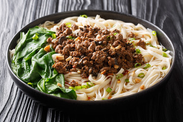 Spicy Dan Dan Noodles with minced meat and herbs served with hot sauce in a plate. horizontal