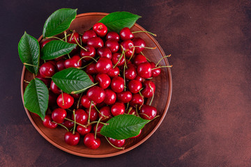 Sweet fresh organic cherry background close-up. Cherry in the plate with leaves on a dark background