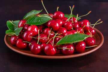 Sweet fresh organic cherry background close-up. Cherry in the plate with leaves on a dark background