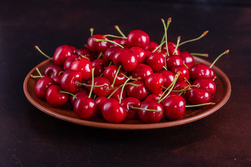 Sweet fresh organic cherry background close-up. Cherry in the plate with leaves on a dark background