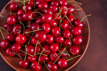 Obraz na płótnie Canvas Sweet fresh organic cherry background close-up. Cherry in the plate with leaves on a dark background