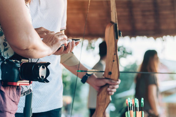 Tourists try to use a bow and arrow and shoot at a target in the amusement park.