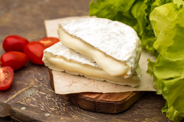 White mold cheese on a cutting board. Tomatoes and fresh lettuce. brie cheese. Tasty camembert