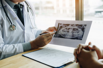 Dentist hand holding pen pointing x-ray picture and talking to the patient about medication and surgery treatment.
