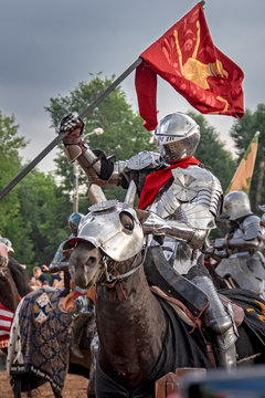 Knight on horseback in medieval steel armor with flag.