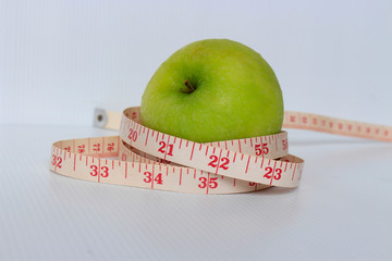 Diet and healthy concept; slimming by apple, good for health. green apple and measure tape with white background