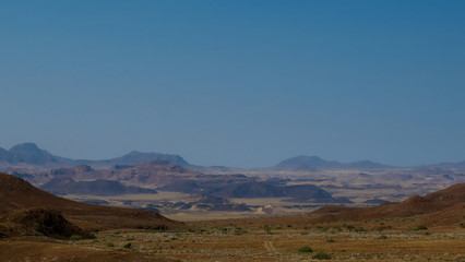 Namibian desert mountains with brown and yellow rock, ostrich in the foreground, dry desolate landscape