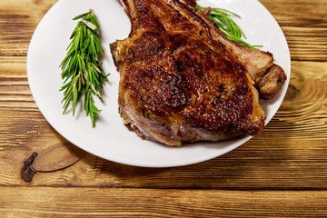 Roasted beef rib eye steak on bone with rosemary in white plate on wooden table