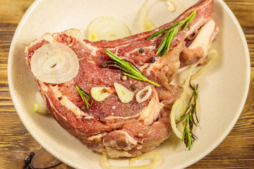 Marinated beef rib eye steak on bone with spices, onion and rosemary on wooden table
