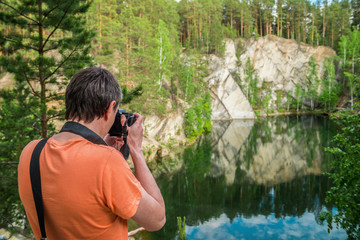 A photographer with a camera takes pictures of nature, against the background of a forest, a pond, rocks