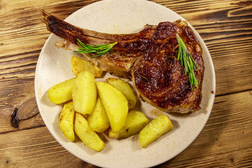 Roasted beef rib eye steak on bone with baked potatoes and herbs on wooden table