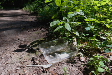 Garbage in the forest, Plastic packaging and a plastic spoon in the forest. Protect the environment . Closeup foliage and road in the forest.