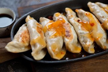 Closeup of asian dumplings with dipping sauces in a cast-iron serving pan, selective focus
