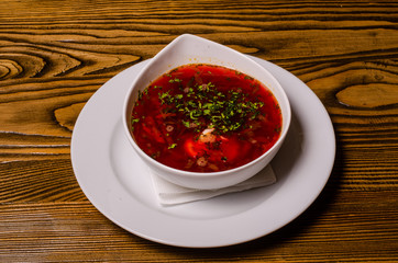 Beats soup, borsch with sour cream; bead and pickles on a background. borsch in a white dish, slices of bread on a wooden cutting board, whole pickles in a wooden dish.