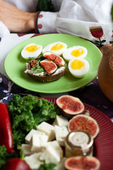 A gourmet lunch: a rye bread sandwich, cheese bites, sliced figs and boiled eggs.