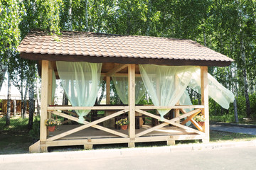 Arbor in a park area among the birches. Green transparent blinds and flower pots..