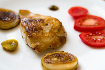Grilled fish, fillet with roasted onion, sliced tomato and slices of jalapeno peppers.