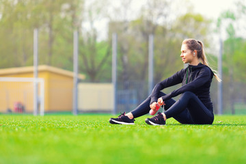 young pretty thirsty blonde Caucasian girl in suit resting after sport run in the park on football...