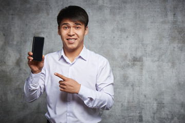 Joyful Asian pointing at mobile phone with index finger advertising something. Attractive kazakh in...