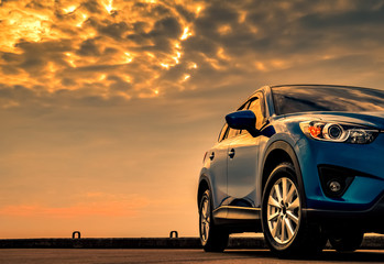 Blue compact SUV car with sport and modern design parked on concrete road by the sea with beautiful sunset sky.  Hybrid and electric car technology concept. Car parking space. Automotive industry. - obrazy, fototapety, plakaty