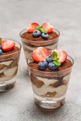 Classic tiramisu dessert with blueberries and strawberries in a glass on concrete background