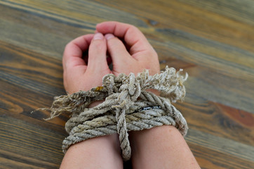 Woman's hands tied with an old rope, the rope is gray with age and unraveling at the ends. It is...