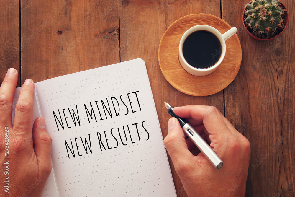 Poster top view image of table with open notebook and the text new mindset new results. success and persona