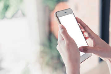 Croppes shot women hand holding white smartphone with blank screen on wooden counter bar in cafe. vintage tone for business technology background concept. closeup white mock up mobile.
