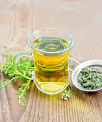 Tea of thyme in mug with strainer on old wooden board