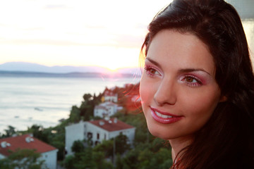 Jolie jeune femme brune devant un coucher de soleil et la mer