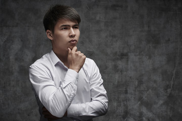 Serious Asian businessman ithinking of taking a loan on black background in white shirt. Kazakh student