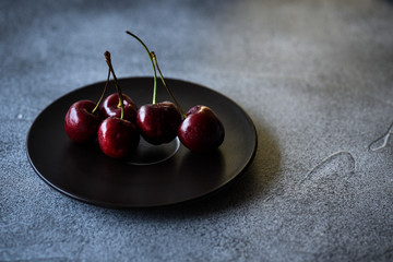 Red sweet cherries on a black plate on a dark surface.