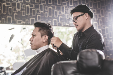 Portrait of barber making hair cut of his attractive man in barbershop