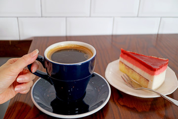Woman's Hand Holding Cup of Hot Coffee with Raspberry Mousse Cake Served on Wooden Table