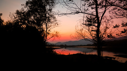 Landscape with orange and purple at sunset  silhouettes of mountains, hills and forest lake