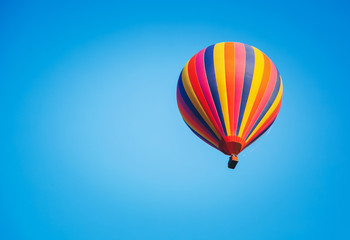 Fototapeta na wymiar Bright striped multicolored balloon in the blue sky, freedom of travel adventure