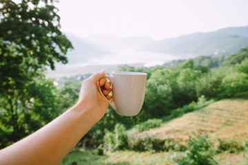 Hand with a cup of tea over mountains and lake in Georgia